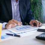 Person working on financial reports at desk with tablet and notepad